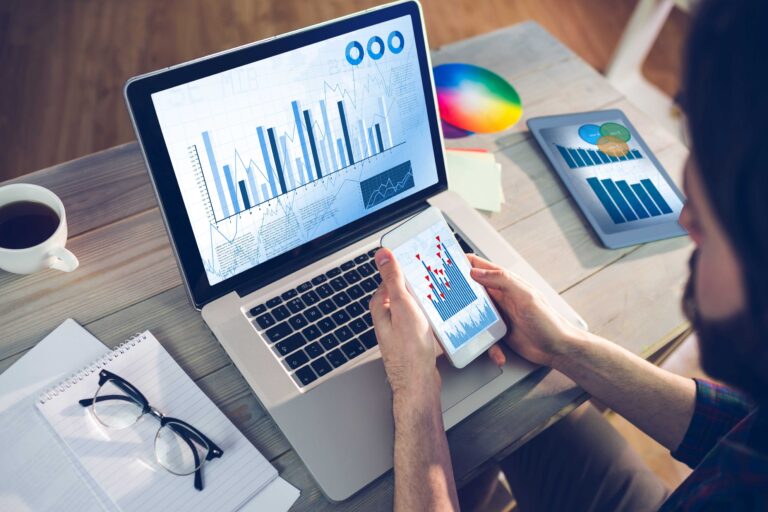 A man analysing data on multiple electronic devices.